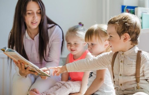 Opiekunka czyta książkę trójce małych dzieci siedzących obok niej