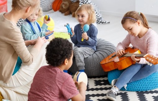 Dzieci grają na instrumentach muzycznych podczas zajęć z opiekunką w sali żłobka